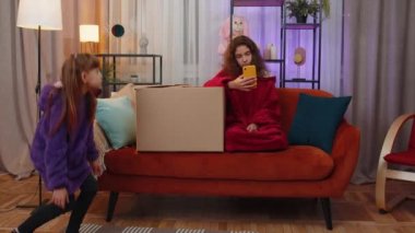 Little girls playing hide and seek, peekaboo game. Hiding inside cardboard box. Toddler child searching looking for sister, having no idea where is she. Three siblings children kids or friends at home