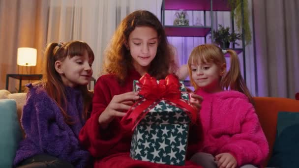 ハッピーティーンの女の子と幼児の子供の姉妹は 興奮した驚きの顔でクリスマスギフトボックスを開きます 女性3人の子供兄弟や友人保持光輝く誕生日プレゼントでホームプレイルーム — ストック動画