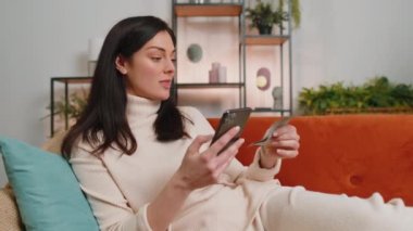 Planning family budget. Young happy brunette woman counting money dollar cash use smartphone calculate domestic bills at home. Joyful girl satisfied of income saves money for planned vacation gifts