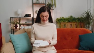 Stressed brunette woman at living room looking at unpaid bank debt bills, doing paperwork, planning budget, calculate finances mortgage payments, deadline. Girl throws paper bills at home apartment
