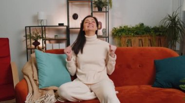 Money cash dollar rain falling on young woman celebrating success, winning, goal achievement, good news, lottery jackpot luck, dream come true at home apartment indoors. Career grow. Girl sits on sofa