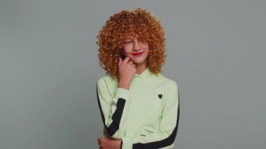 Cheerful lovely young child girl kid in glasses smiling looking at camera. Funny female teenager children schoolgirl with curly frizzy hair isolated portrait alone on studio gray background. Childhood