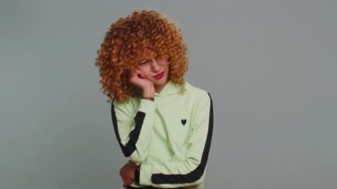 Dental problems. Young curly hair child girl kid touching cheek, closing eyes with expression of terrible suffer from painful toothache, sensitive teeth, cavities. Teenager children on gray background