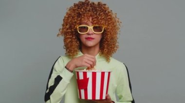 Excited young teenager school girl in 3D glasses eating popcorn, watching interesting tv serial, sport game, film, online social media movie content. Curly haired child kid on studio gray background