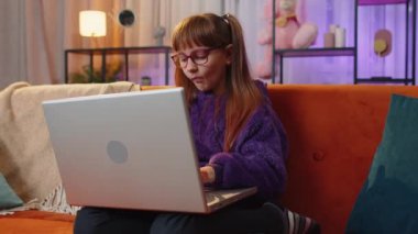 Toddler little girl sits on couch closing laptop after finishing education in play room at home. Teen child kid freelancer study online, remote work. E-learning, browsing internet on notebook computer