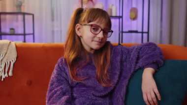 Happy calm teen toddler girl child kid 7 years old smiling friendly, glad expression looking at camera dreaming resting, relaxation feel satisfied concept good news on couch. Teen children at home