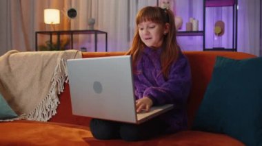 Toddler girl sitting on couch, looking at camera, making video webcam conference call with friends or family, enjoying pleasant conversation. Teen teenager child, kid laughing waving hello at home