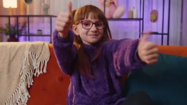 Like. Happy toddler teen girl looking approvingly at camera showing thumbs up, like sign positive something, good great news, positive feedback. Young child, kid sitting on couch at home living room