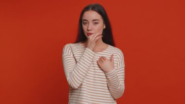 I will not say anyone. Frightened woman closing her mouth with hand, looking intimidated scared at camera, gestures no, refusing to tell terrible secret, unbelievable truth. Girl on red background