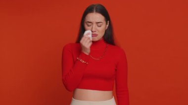 Upset disappointed pretty young woman in crop top wipes tears and cries from despair being sad because of unfair things. Millennial girl in depression, despair, loss isolated on red studio background