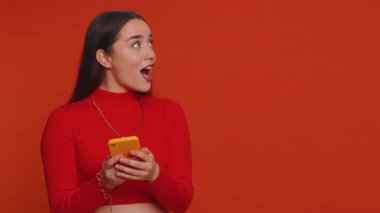 Woman using smartphone pointing empty place, advertising area for commercial text, copy space for goods application promotion social networks positive feedback. Girl isolated on red studio background