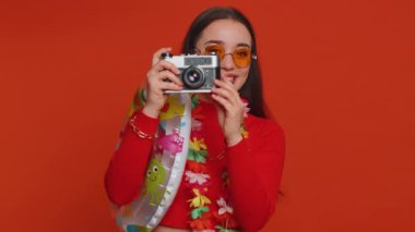 Happy young woman tourist photographer in sunglasses taking pictures photos on retro camera. Travel, summer holiday vacation, trip to seaside. Lovely smiling girl traveler on studio red background
