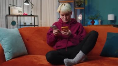 Planning family budget. Young woman with short hair counting money dollar cash use smartphone calculate domestic bills at home. Joyful girl satisfied of income saves money for planned vacation gifts