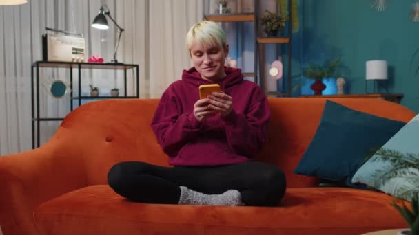 Woman Short Blonde Hair Sitting Sofa Uses Mobile Phone Smiles — 图库视频影像
