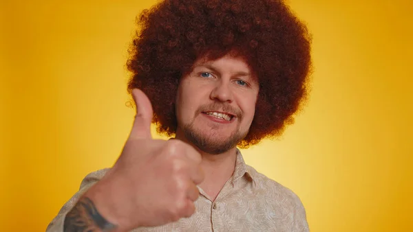 Great job, nice. Cheerful positive happy bearded man with afro hairstyle showing thumbs up, nodding in approval, successful good work. Young stylish guy on yellow background. People sincere emotions