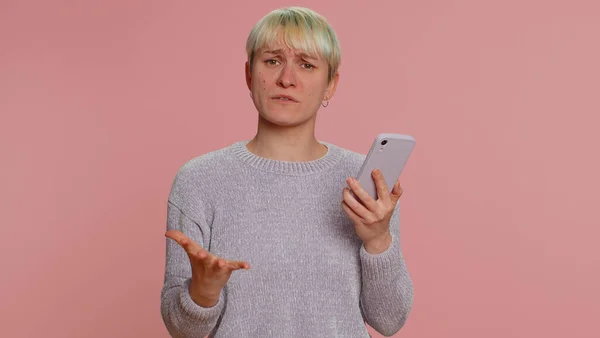 Hipster woman with short hair use mobile cell phone typing browsing, loses becoming surprised sudden lottery results, bad fortune, loss, fail. Young girl isolated alone on pink studio wall background