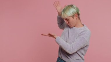 Lovely one millennial woman showing thumbs up and pointing empty place, advertising area for commercial text, copy space for goods promotion. Young girl on pink background. Lgbt gay lesbian people