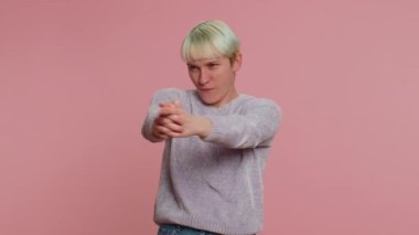 Woman with short hair pointing around with finger gun gesture, looking confident, making choice, shooting killing with hand pistol right on target. Girl on pink background. Lgbt gay lesbian people