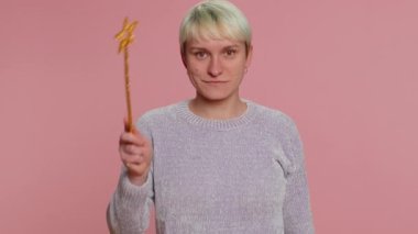 Magician witch woman gesturing with magic wand fairy stick, making wish come true, casting magician spell, advertising holidays sale discount. Girl on pink studio background. Lgbt gay lesbian people