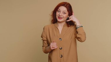 Call us, here is contact number. Young pretty redhead woman in blouse looking at camera doing phone gesture like says hey you call me back, conversation. Caucasian girl isolated on beige background