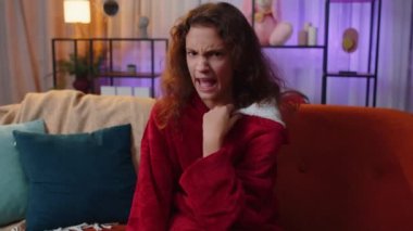 Hoşlanmamak. Sinirli kız işaret dilini gösteriyor, hoşnutsuzluğunu dile getiriyor, hoşnutsuzluğunu dile getiriyor, modern ev dairelerinde tatminsiz kötü işler yapıyor. Tatminsiz bir çocuk, oturma odasında kanepede bir çocuk.