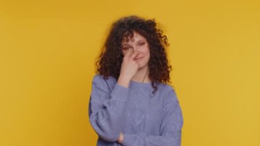 I am watching you. Caucasian woman pointing at her eyes and camera, show I am watching you gesture, spying on someone. Young adult curly haired girl isolated alone on yellow studio wall background