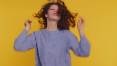 Funny joyful sincere woman 20 years old making playful silly facial expressions and grimacing, fooling around showing tongue. Young lovely curly haired girl isolated alone on yellow wall background