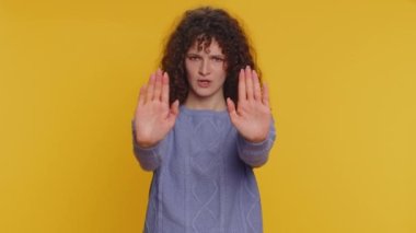 Stop. Curly haired woman say No hold palm folded crossed hands in prohibited access gesture, warning of finish, declining communication, body language danger. Young girl isolated on yellow background