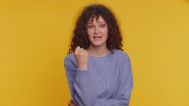Aggressive angry curly haired woman trying to fight at camera, shaking fist, boxing with expression, punishment, disappointment, rage, quarrel. Young teen girl isolated on yellow studio background