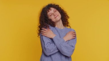 Come to me, I want to embrace you. Happy smiling curly haired woman spread hands and give hug to you. Pleasant expression, love feelings. Young teen girl isolated alone on yellow studio background