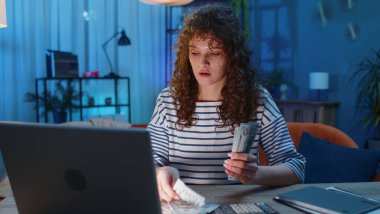 Planlama bütçesi. Masada oturan zengin genç kadın nakit sayıyor. Ev faturalarını dizüstü bilgisayarla hesaplıyor. Kazancından memnun bir kız, planlı hediyeler için ev ofisinden para biriktiriyor.