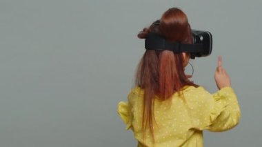 Rear view of toddler girl in VR glasses using virtual reality futuristic technology VR app headset helmet to play simulation 3D 360 video game. Child kid isolated on gray background. Little children