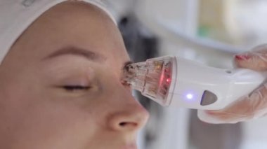 Güzellik uzmanı, kadınlara güzellik merkezinde yüz ve göz çevresi kaldırma prosedürü, kolajen maskesi yaptırıyor. Kozmetik uzmanı vakum yüz masajı terapisi için elektrikli ekipman kullanıyor. Güzellik tedavisi. Dikey