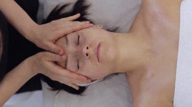 Terapist kadın, elleriyle spa masajı yaptırıyor. Salonda pürüzsüz, sağlıklı cilt bakımı. Detoks ve iyileşme. Yüz fizyolojisi seansında müşteri. Dikey görünüm