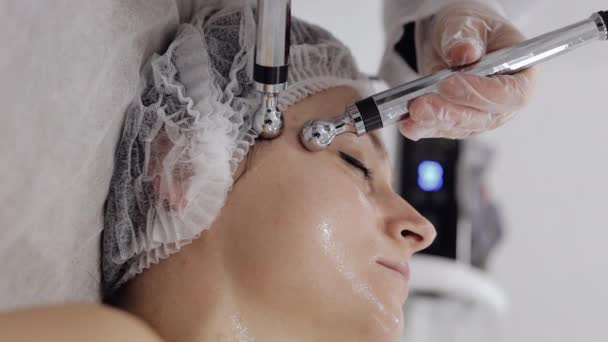 美容师让女人面对小电流疗法 女孩皮肤护理在温泉诊所抗老化 美容师医生使用电脉冲进行面部美容治疗 纵向观点 — 图库视频影像