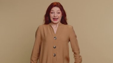 Bluz giymiş neşeli kızıl saçlı kadın bağırarak, el kol hareketi yaparak başarıyı, kazananı, doğum gününü, piyango vurgununu hedefleyen başarılıları kutladım. Bej renkli stüdyo arka planında yetişkin bir kız