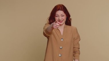Amused redhead woman pointing finger to camera, laughing out loud, taunting making fun of ridiculous appearance, funny joke anecdote. Young ginger girl isolated alone on beige studio background