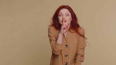 Shh be quiet please. Portrait of millennial woman 20 years old presses index finger to lips makes silence gesture sign do not tells secret. Young lovely redhead girl posing on beige studio background