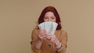 Zengin patron milenyum kadını hayran, başarılı iş kariyeri, piyango talihlisi, büyük gelir ve servet gibi banknotlar sallıyor. Genç kızıl saçlı kız bej arka planda izole edilmiş.