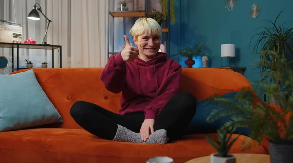 Like. Happy woman with short hair looking approvingly at camera showing thumbs up, like sign positive something, good great news, positive feedback. Adult girl sitting on couch at home living room