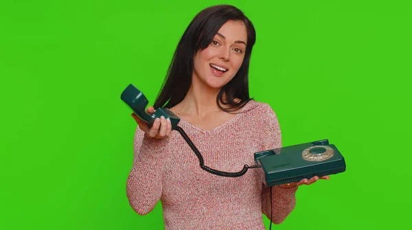 Hey you, call me back. Young woman in sweater talking on wired vintage old-fashioned retro telephone of 80s, says hey you call me back. Girl working in call center isolated on chroma key background