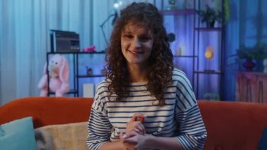 Kıvırcık saç stili olan güzel, neşeli bir kadın önerini çok onaylıyor, başını sallıyor, kaliteli bir işten memnun, evlenme teklifi gibi. Gece odasındaki kanepede oturan genç kız.