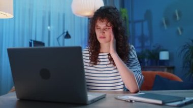 Yorgun, genç, serbest çalışan bir kadın dizüstü bilgisayar kullanıyor. Baş ağrısı, tansiyon, migren, evde stres. Kız defter üzerinde çalışıyor, mesajlar gönderiyor, online alışverişler yapıyor, film seyrediyor.