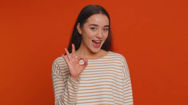 Ok. Joyful happy pretty woman in pullover looking approvingly at camera showing approve feedback gesture like sign positive something good. Young girl on red studio background. People sincere emotion