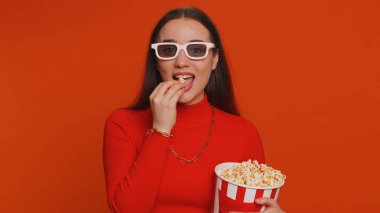 Üç boyutlu gözlüklü, patlamış mısır yiyen ve ilginç TV dizileri, spor oyunları, filmler, çevrimiçi sosyal medya filmi içerikleri izleyen heyecanlı bir kadın. Kırmızı arka planda eğlenen kız