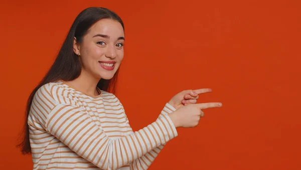 Lovely woman in pullover showing thumbs up and pointing empty place, advertising area for commercial text, copy space for goods promotion. Young pretty girl. Indoor studio shot on red wall background