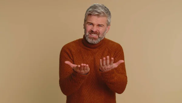 Middle-aged man in sweater screams yell from stress tension problems feels horror hopelessness fear panic surprise shock expresses gestures rage. Senior mature guy isolated on beige studio background