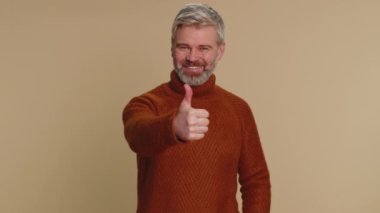 Like. Mature middle-aged man in sweater raises thumbs up agrees with something or gives positive reply recommends advertisement likes good. Senior elderly guy isolated alone on beige studio background