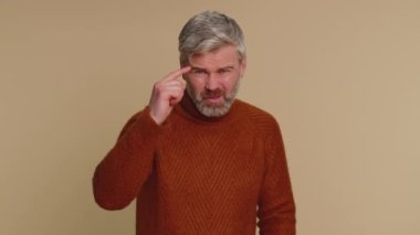 Sen delisin, aklın yerinde değil. Orta yaşlı yaşlı bir adam kamerayı işaret edip aptalca bir hareket yapıyor ve bir aptalı delice plan için suçluyor. Yaşlı yetişkin adam bej renkli stüdyo arka planında tek başına izole edilmiş.