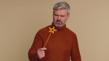 Magician wizard man gesturing with magic wand fairy stick, making wish come true, casting magician spell, advertising holidays sale discount. Senior adult guy isolated on beige studio background